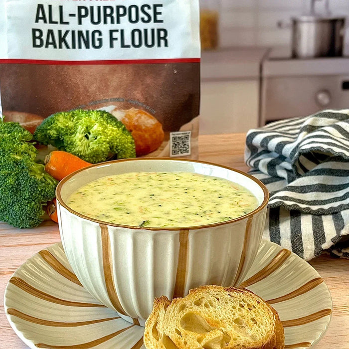 Broccoli & cheddar soup served in a bowl with crusty bread on the side