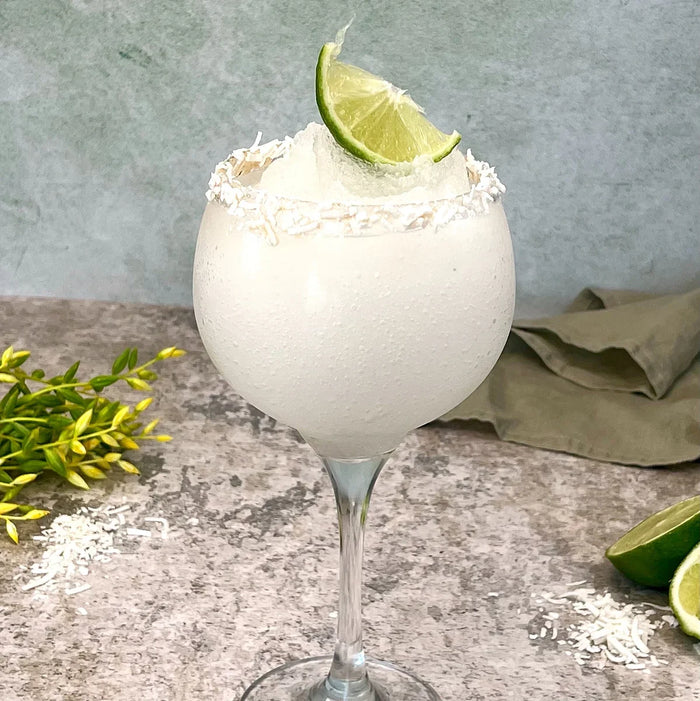 Frozen coconut margarita in a stemmed glass with shredded coconut rim and lime garnish.