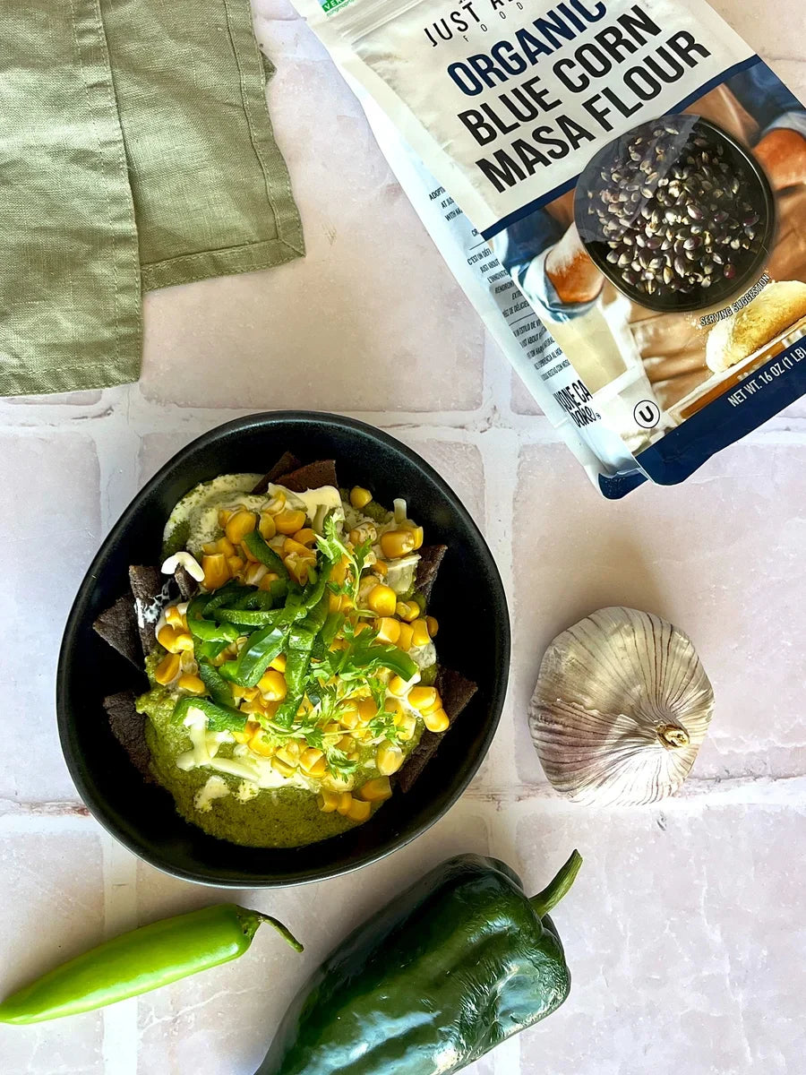 Blue corn chilaquiles in black bowl with green poblano sauce, corn, peppers and herbs.