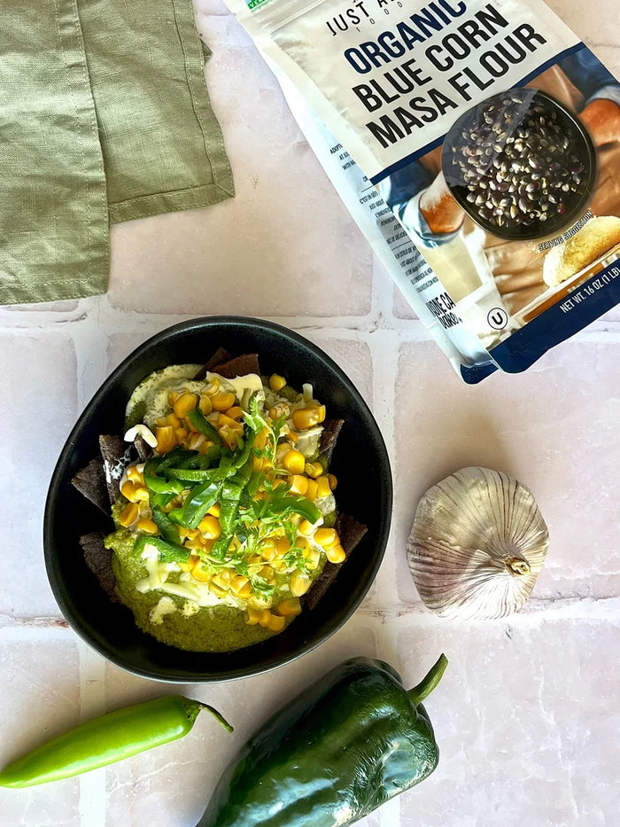 Blue corn chilaquiles in black bowl with green poblano sauce, corn, peppers and herbs.
