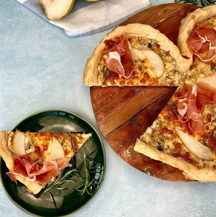 Pear, prosciutto and gorgonzola pizza slices on wooden board.