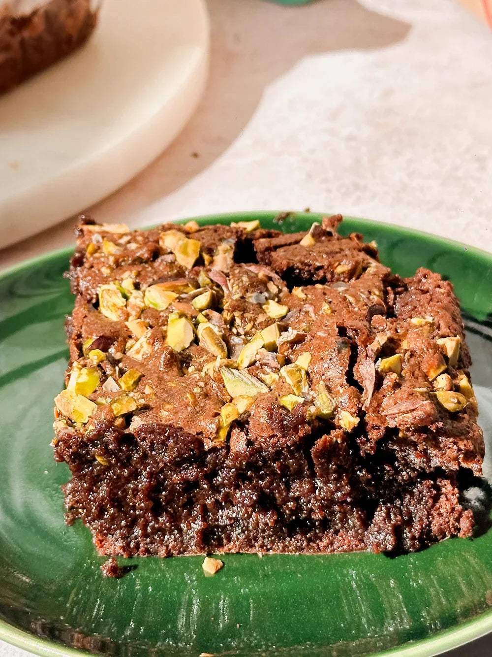 Chocolate pistachio brownie topped with chopped pistachios served on a green plate