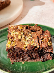 Chocolate pistachio brownie topped with chopped pistachios served on a green plate